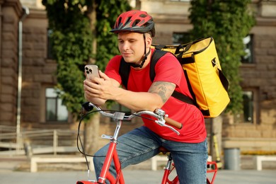 Photo of Courier with thermo bag and smartphone on bicycle outdoors. Food delivery service