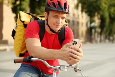 Photo of Courier with thermo bag and smartphone on bicycle outdoors. Food delivery service