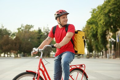 Photo of Courier with thermo bag riding bicycle outdoors. Food delivery service