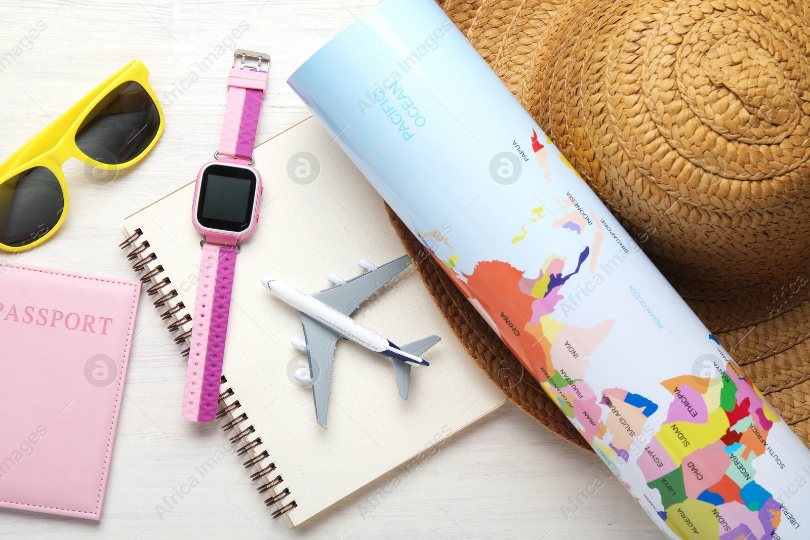 Photo of Time for summer vacation. Toy plane, passport, notebook, smart watch, world map and beach accessories on light wooden table, flat lay