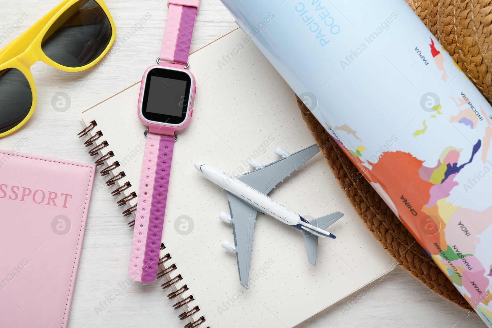 Photo of Time for summer vacation. Toy plane, passport, notebook, smart watch, world map and beach accessories on light wooden table, flat lay