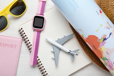 Photo of Time for summer vacation. Toy plane, passport, notebook, smart watch, world map and beach accessories on light wooden table, flat lay