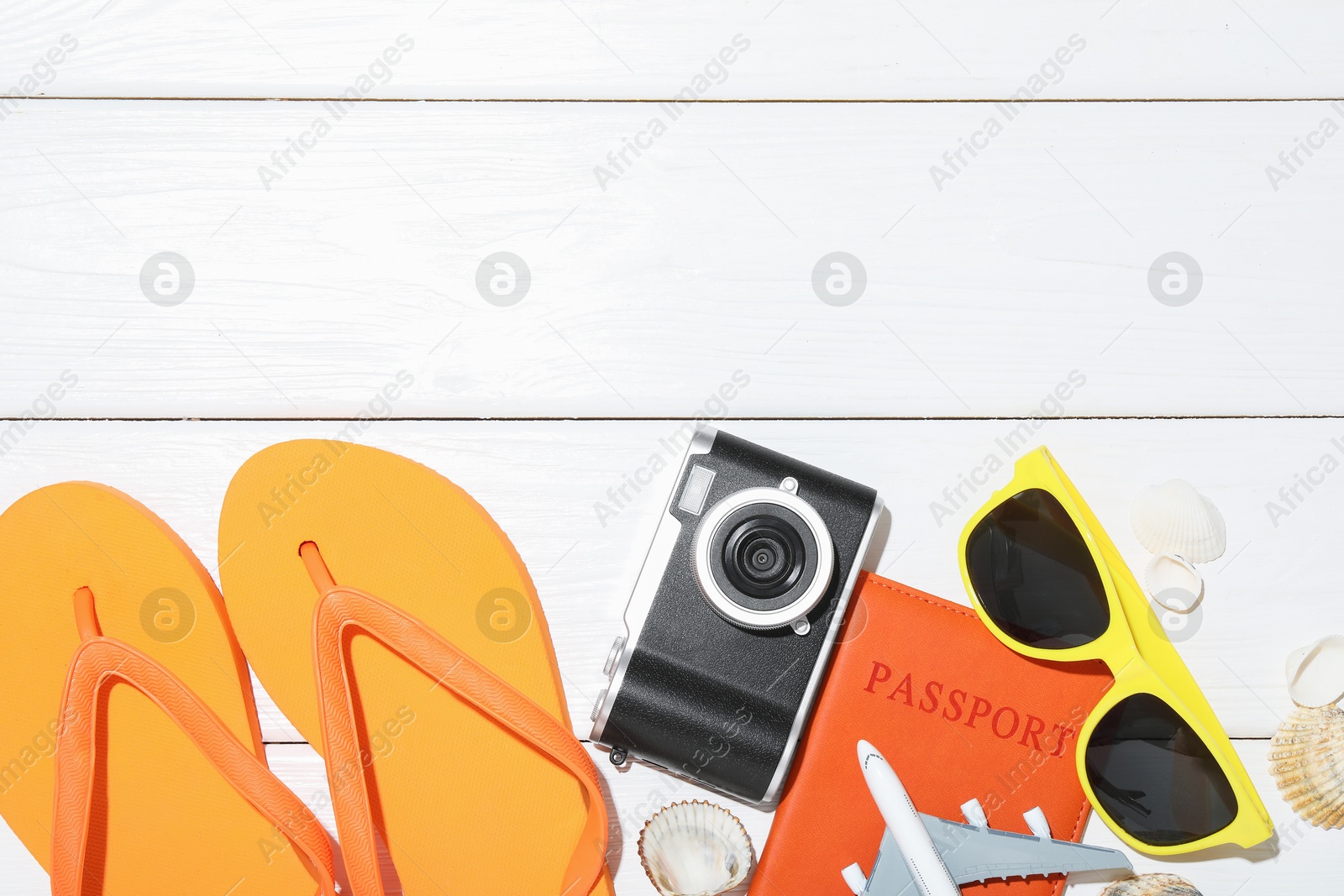 Photo of Time for summer vacation. Toy plane, passport, camera and beach accessories on white wooden table, flat lay. Space for text