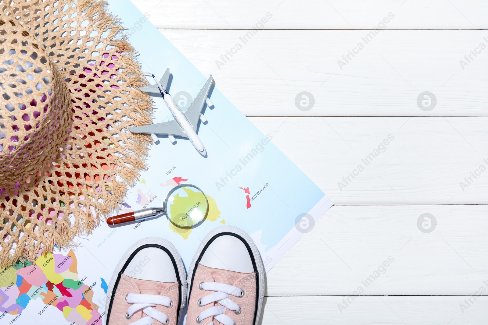Photo of Time for summer vacation. Toy plane, magnifying glass, shoes, straw hat and world map on white wooden table, flat lay. Space for text