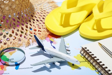 Photo of Time for summer vacation. Toy plane, stationery, magnifying glass and beach accessories on world map, closeup