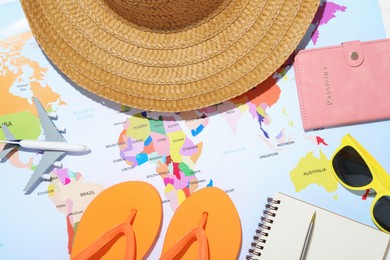 Photo of Time for summer vacation. Passport, stationery, toy plane and beach accessories on world map, flat lay