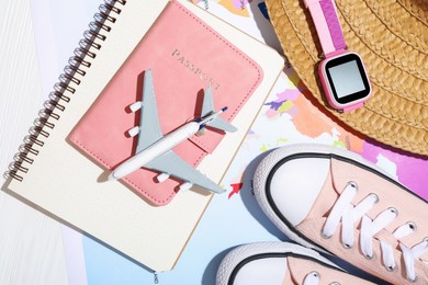 Photo of Time for summer vacation. Passport, notebook, toy plane, smart watch, shoes, straw hat and world map on white wooden table, flat lay