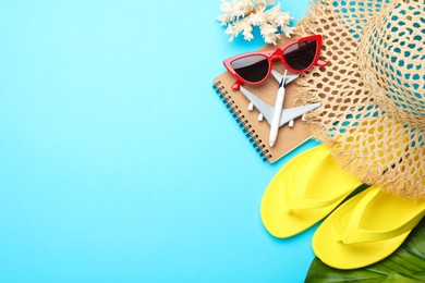 Photo of Time for summer vacation. Notebook, toy plane, green leaf and beach accessories on light blue background, flat lay. Space for text