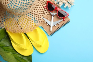 Photo of Time for summer vacation. Notebook, toy plane, green leaf and beach accessories on light blue background, flat lay. Space for text