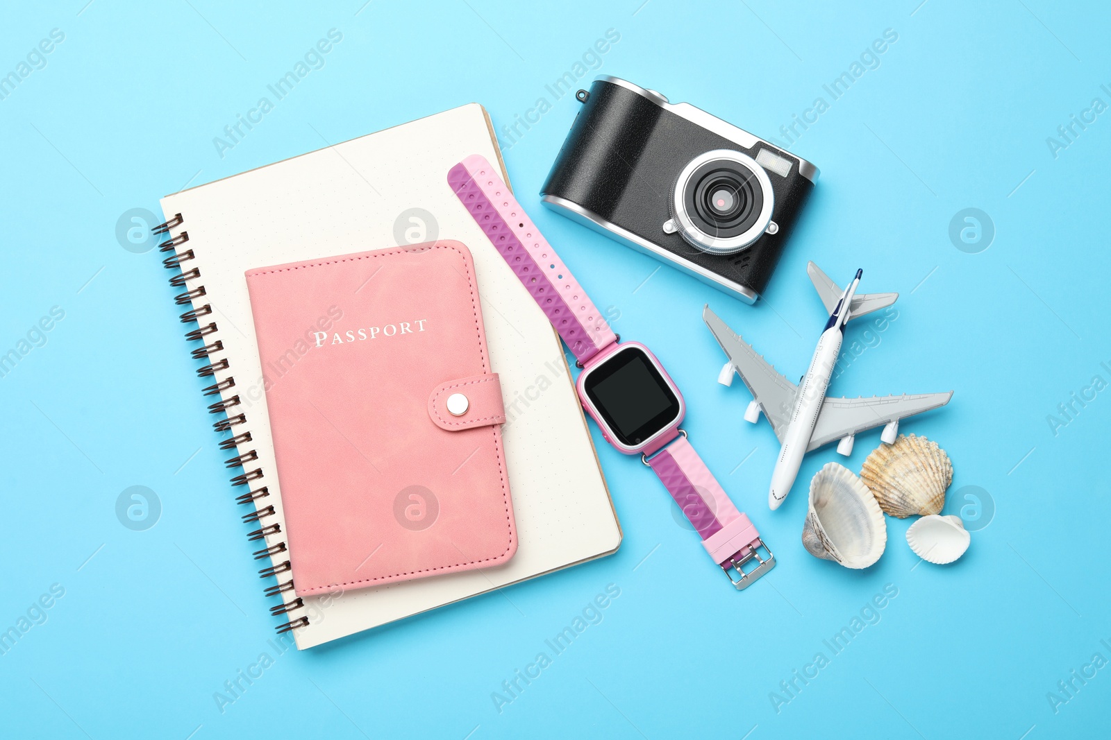 Photo of Time for summer vacation. Passport, notebook, toy plane, camera, smart watch and seashells on light blue background, flat lay