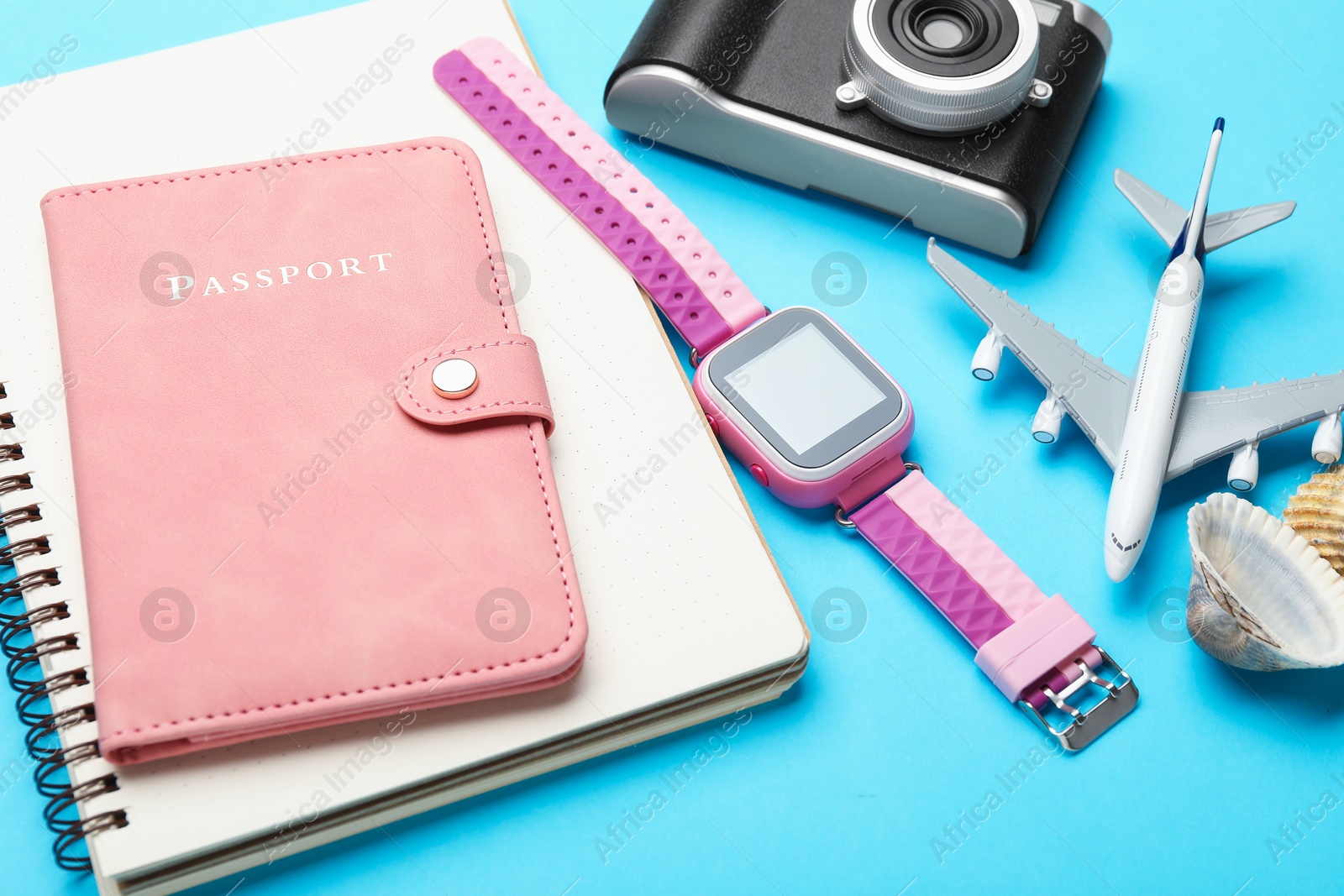 Photo of Time for summer vacation. Passport, notebook, toy plane, camera, smart watch and seashells on light blue background, closeup