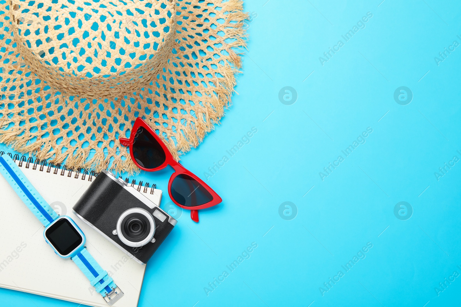 Photo of Time for summer vacation. Camera, smart watch, notebook and beach accessories on light blue background, flat lay. Space for text