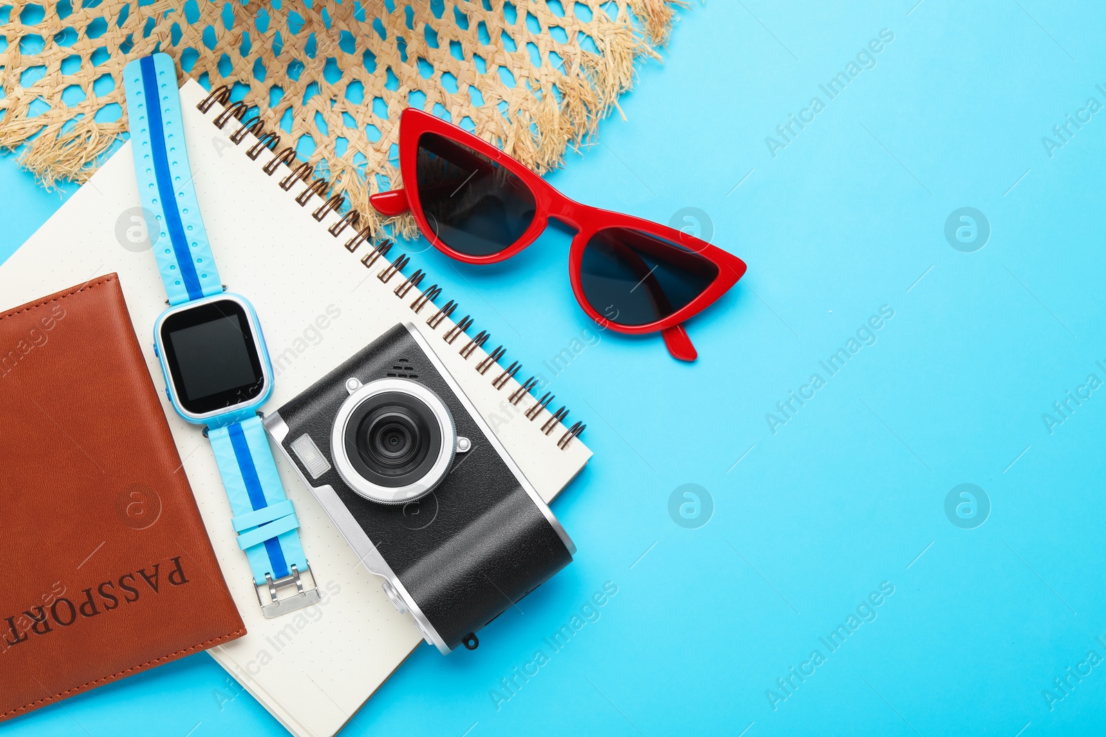 Photo of Time for summer vacation. Camera, smart watch, passport, notebook and beach accessories on light blue background, flat lay. Space for text