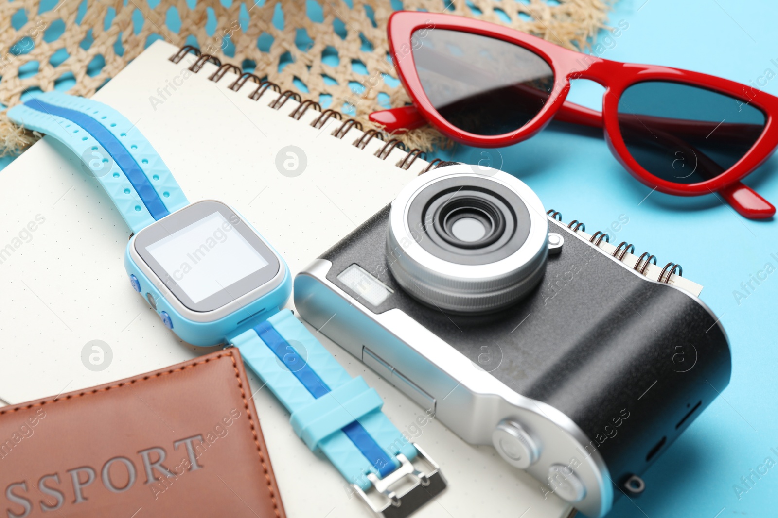 Photo of Time for summer vacation. Camera, smart watch, passport, notebook and beach accessories on light blue background, closeup