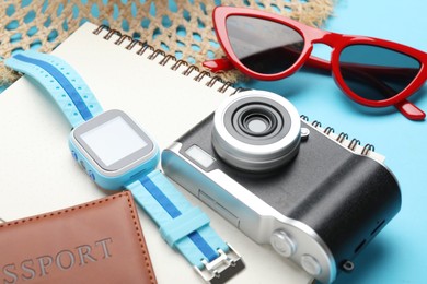 Photo of Time for summer vacation. Camera, smart watch, passport, notebook and beach accessories on light blue background, closeup