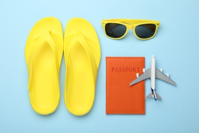 Photo of Time for summer vacation. Toy plane, passport, flip flops and sunglasses on light blue background, flat lay