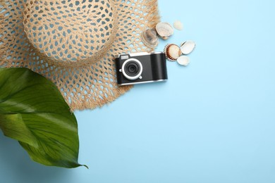 Photo of Time for summer vacation. Camera, seashells, straw hat and green leaf on light blue background, flat lay. Space for text