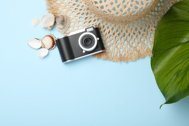 Photo of Time for summer vacation. Camera, seashells, straw hat and green leaf on light blue background, flat lay. Space for text
