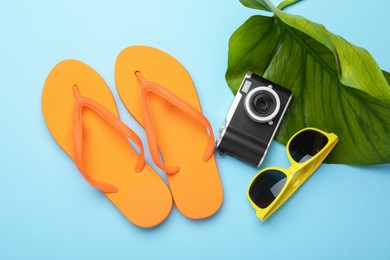 Photo of Time for summer vacation. Camera, green leaf and beach accessories on light blue background, flat lay