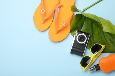 Photo of Time for summer vacation. Camera, green leaf and beach accessories on light blue background, flat lay. Space for text