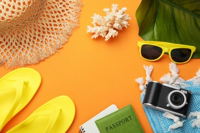 Photo of Time for summer vacation. Passport, notebook, camera, green leaf and beach accessories on orange background, flat lay. Space for text