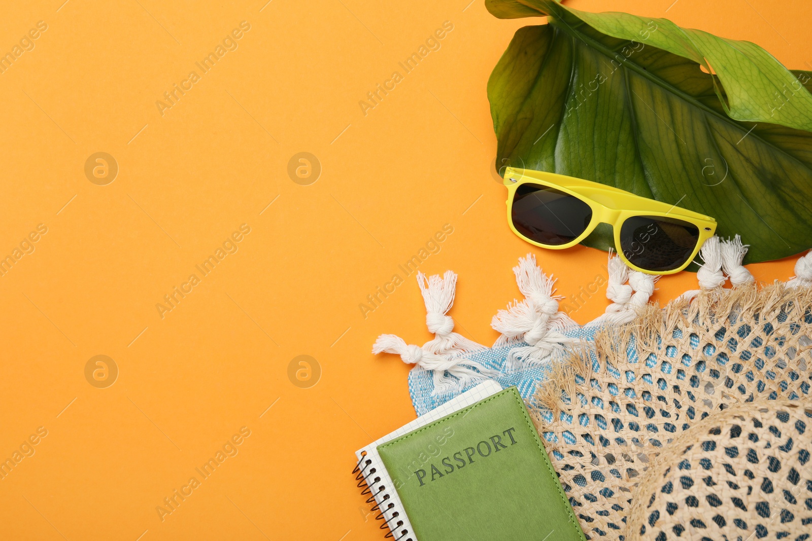 Photo of Time for summer vacation. Passport, notebook, green leaf and beach accessories on orange background, flat lay. Space for text