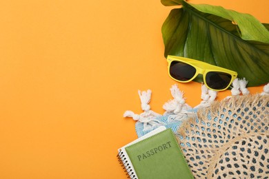 Photo of Time for summer vacation. Passport, notebook, green leaf and beach accessories on orange background, flat lay. Space for text