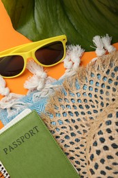 Photo of Time for summer vacation. Passport, notebook, green leaf and beach accessories on orange background, flat lay