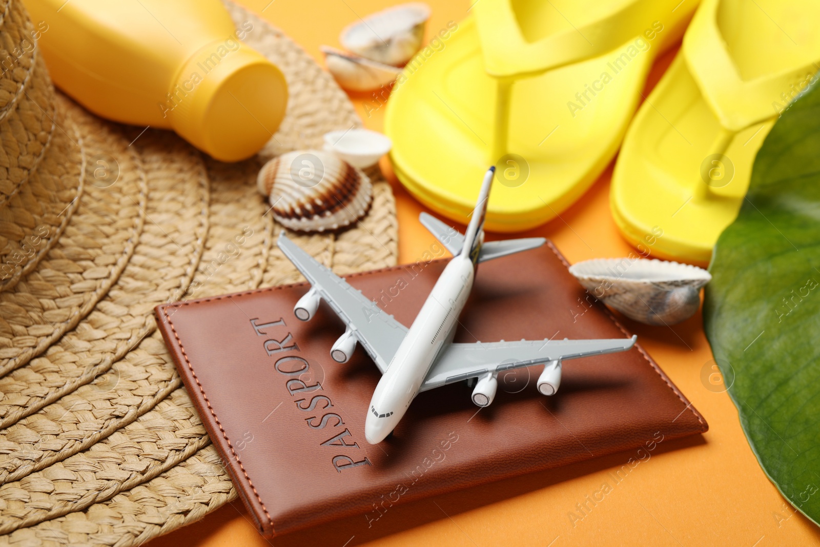 Photo of Time for summer vacation. Passport, toy plane and beach accessories on orange background, closeup