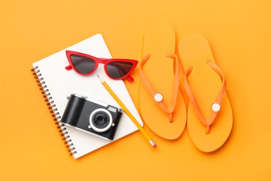 Photo of Time for summer vacation. Camera, notebook, pen and beach accessories on orange background, flat lay
