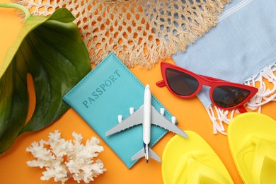 Photo of Time for summer vacation. Passport, toy plane, green leaf and beach accessories on orange background, flat lay