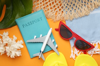 Photo of Time for summer vacation. Passport, toy plane, green leaf and beach accessories on orange background, flat lay
