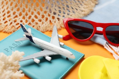 Photo of Time for summer vacation. Passport, toy plane and beach accessories on orange background, closeup