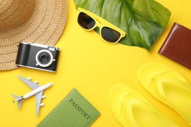 Photo of Time for summer vacation. Passport, camera, toy plane, purse, green leaf and beach accessories on yellow background, flat lay. Space for text