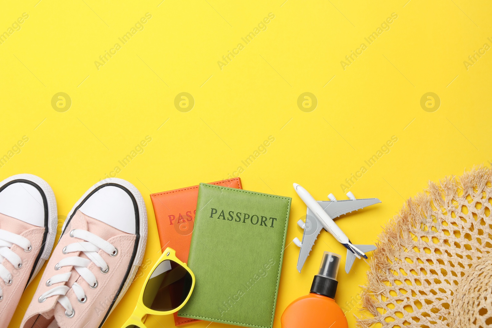 Photo of Time for summer vacation. Toy plane, passports, shoes and beach accessories on yellow background, flat lay. Space for text