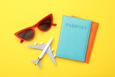 Photo of Time for summer vacation. Toy plane, passports and sunglasses on yellow background, flat lay