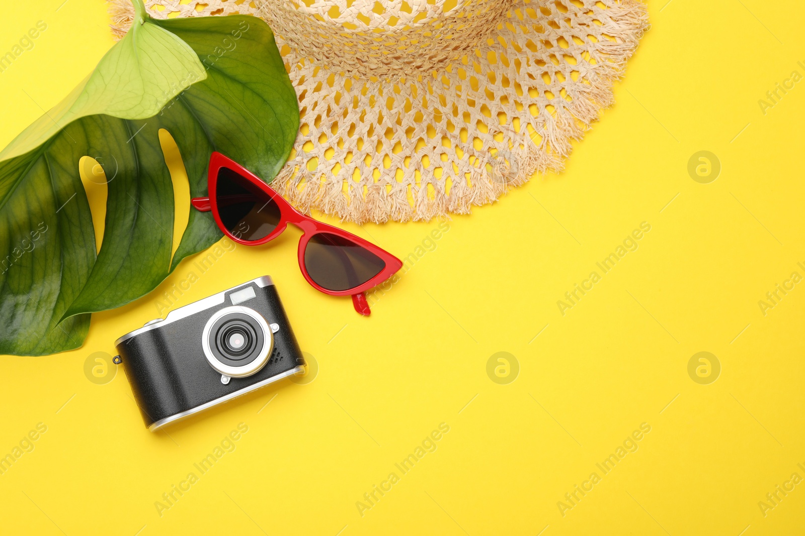 Photo of Time for summer vacation. Camera, sunglasses, straw hat and green leaf on yellow background, flat lay. Space for text