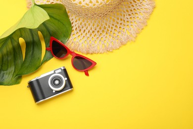 Photo of Time for summer vacation. Camera, sunglasses, straw hat and green leaf on yellow background, flat lay. Space for text