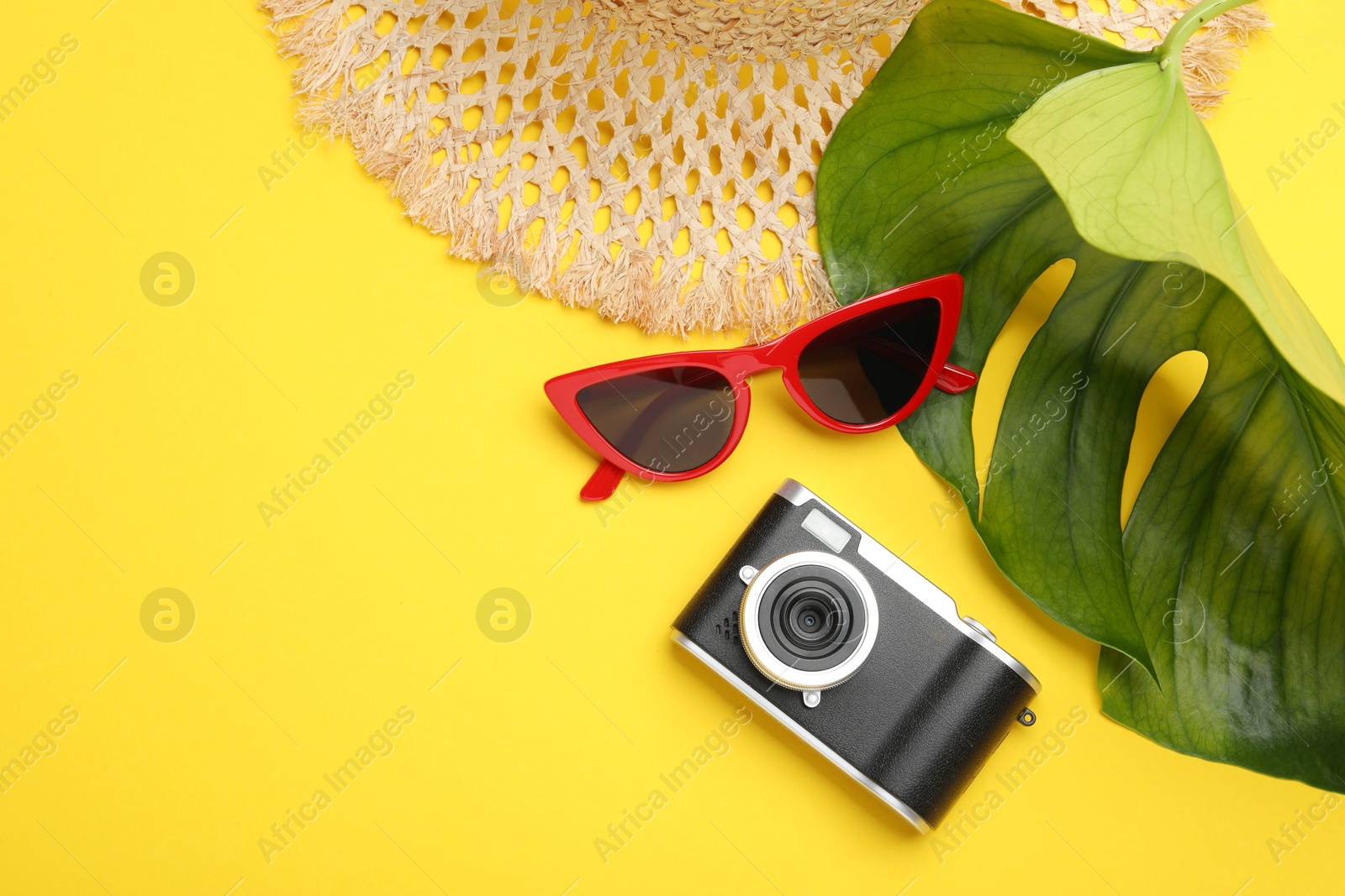 Photo of Time for summer vacation. Camera, sunglasses, straw hat and green leaf on yellow background, flat lay. Space for text