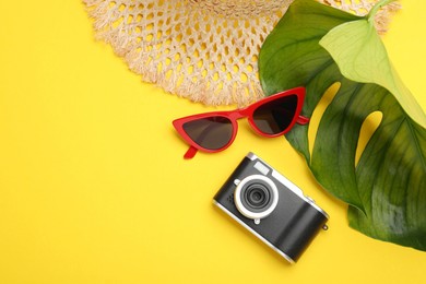 Photo of Time for summer vacation. Camera, sunglasses, straw hat and green leaf on yellow background, flat lay. Space for text