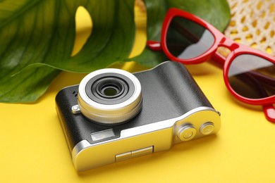 Photo of Time for summer vacation. Camera, sunglasses and green leaf on yellow background, closeup