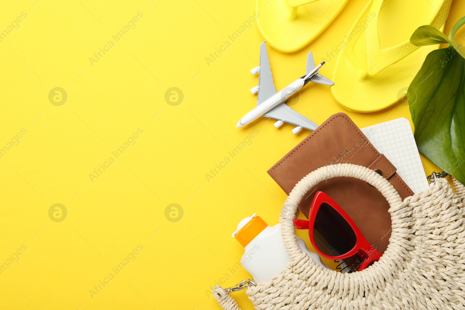 Photo of Time for summer vacation. Passport, notebook, toy plane, beach accessories and green leaf on yellow background, flat lay. Space for text