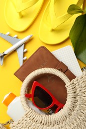 Photo of Time for summer vacation. Passport, notebook, toy plane, beach accessories and green leaf on yellow background, flat lay