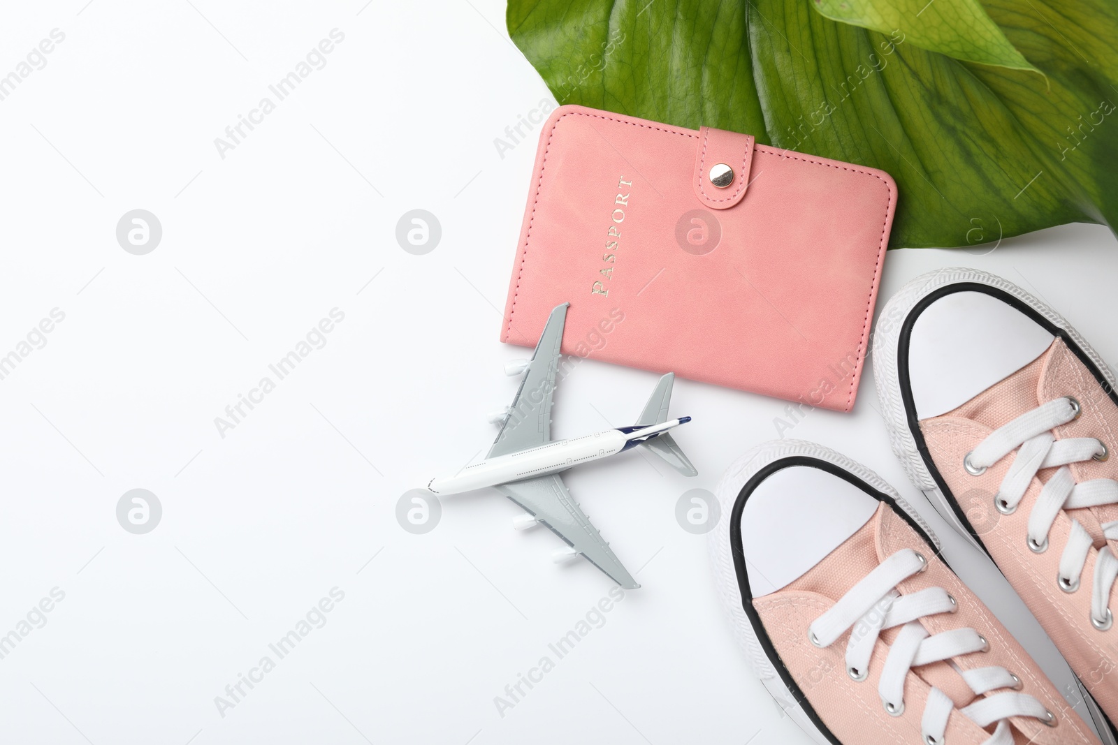 Photo of Time for summer vacation. Passport, toy plane, shoes and green leaf on white background, flat lay. Space for text