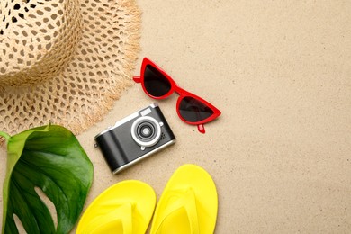 Photo of Time for summer vacation. Camera, green leaf and beach accessories on sand, flat lay. Space for text