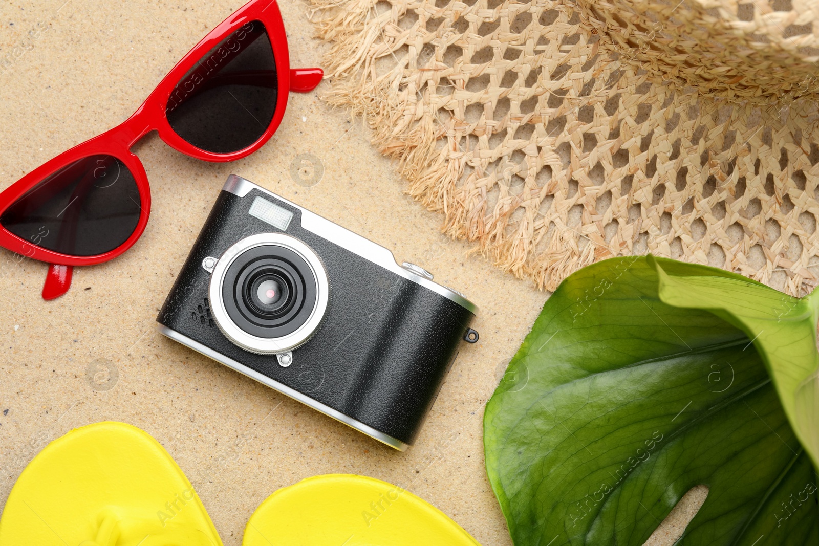 Photo of Time for summer vacation. Camera, green leaf and beach accessories on sand, flat lay