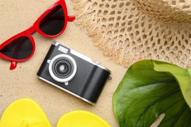 Photo of Time for summer vacation. Camera, green leaf and beach accessories on sand, flat lay