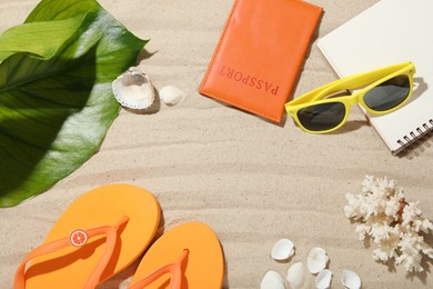 Photo of Time for summer vacation. Passport, notebook, green leaf and beach accessories on sand, flat lay. Space for text
