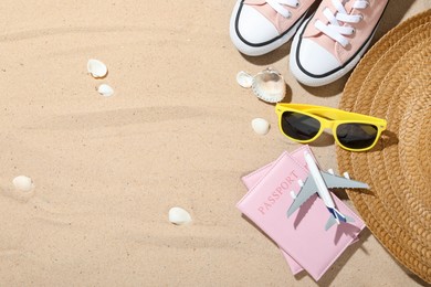 Photo of Time for summer vacation. Toy plane, passports, shoes and beach accessories on sand, flat lay. Space for text