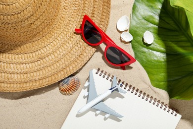 Photo of Time for summer vacation. Toy plane, notebook, green leaf and beach accessories on sand, flat lay